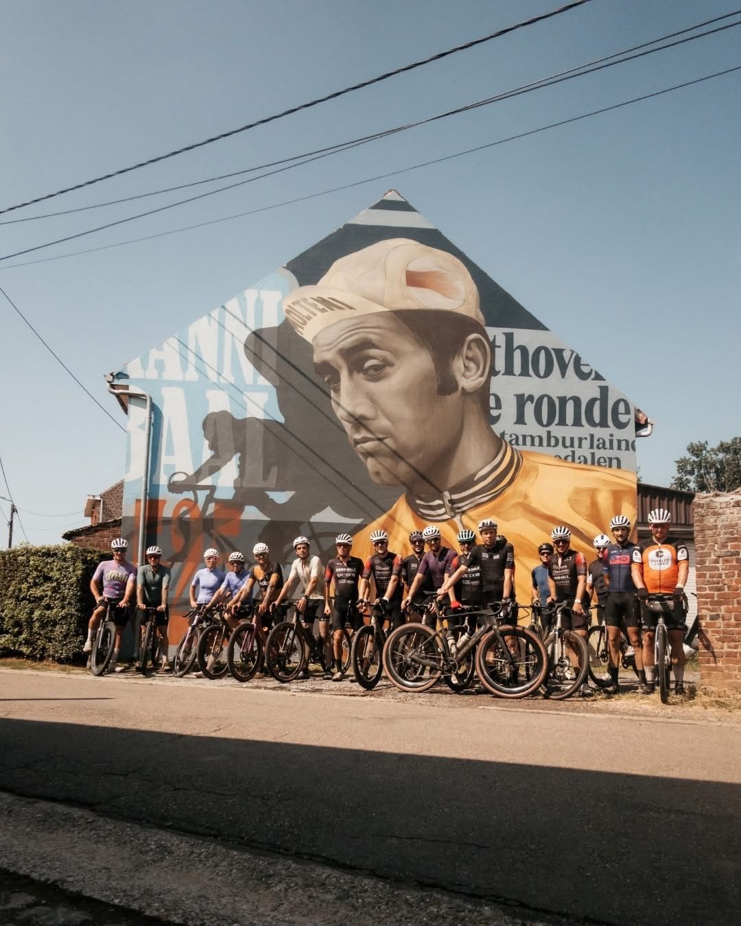 Groep fietsers poseert voor een grote wielermuurschildering